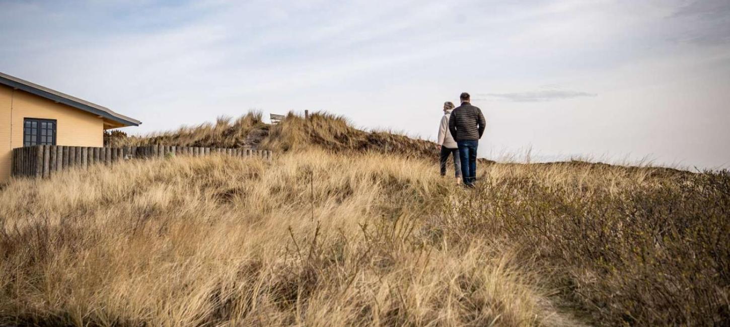 Et par går en tur ved et feriehus i klitlandskab