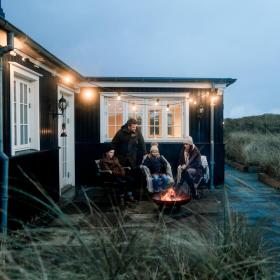 Familie sidder ved bål udenfor sommerhus